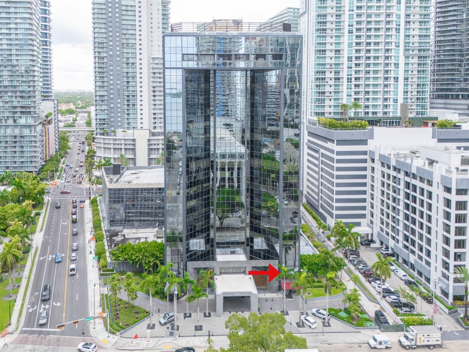 An aerial view shows a modern glass office building with a prominent entrance and landscaping — 1200 Brickell Ave # K, Miami FL 33131, MIAMI, FL