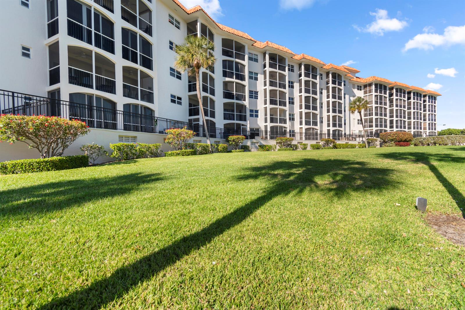 A multi-story white apartment building with screened balconies sits behind a large green lawn — 2871 N Ocean Boulevard # C123, Boca Raton FL 33431, BOCA RATON, FL