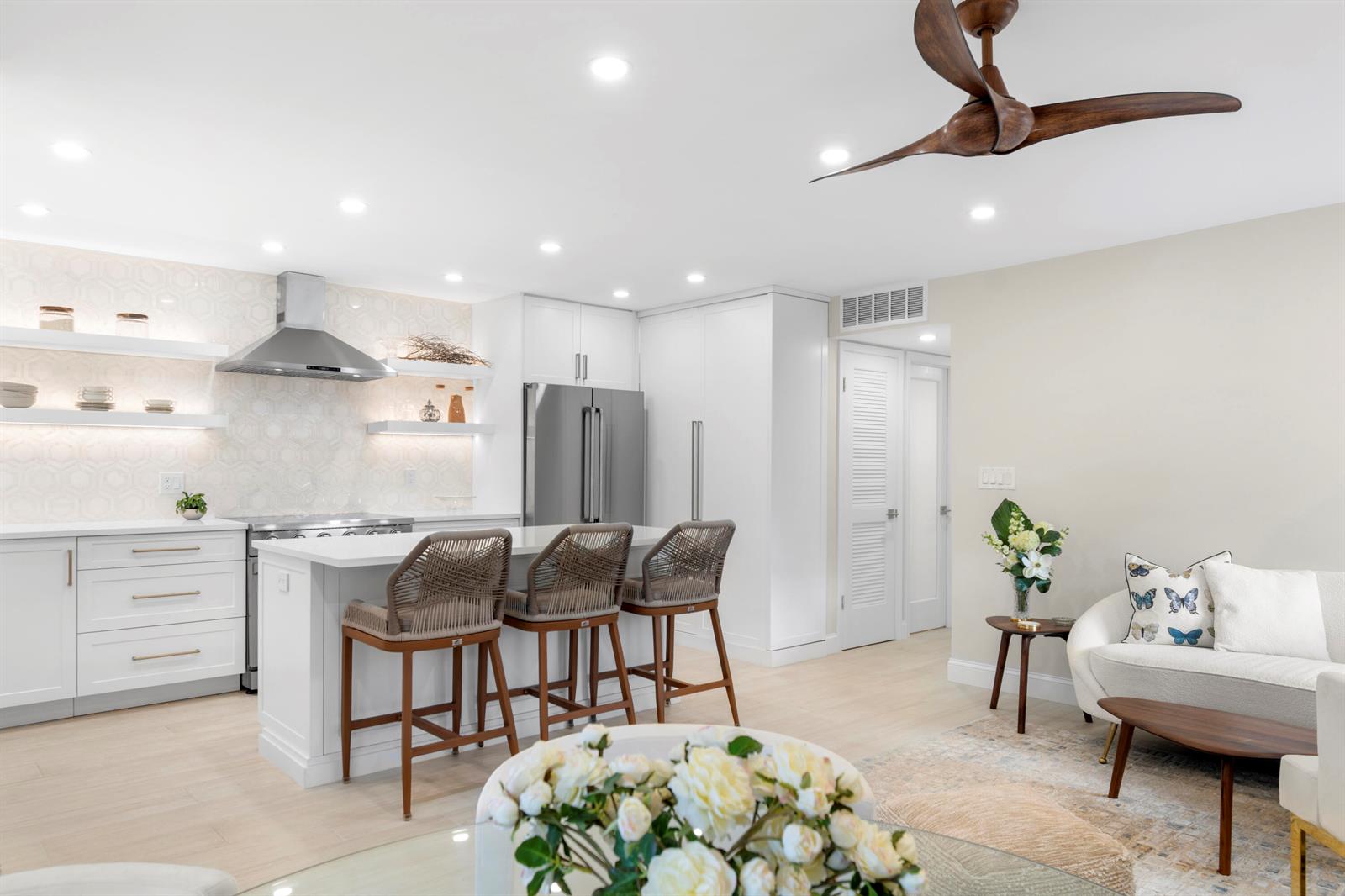 A modern kitchen with white cabinetry, a central island, and bar stools beside a living area — 2871 N Ocean Boulevard # C123, Boca Raton FL 33431, BOCA RATON, FL