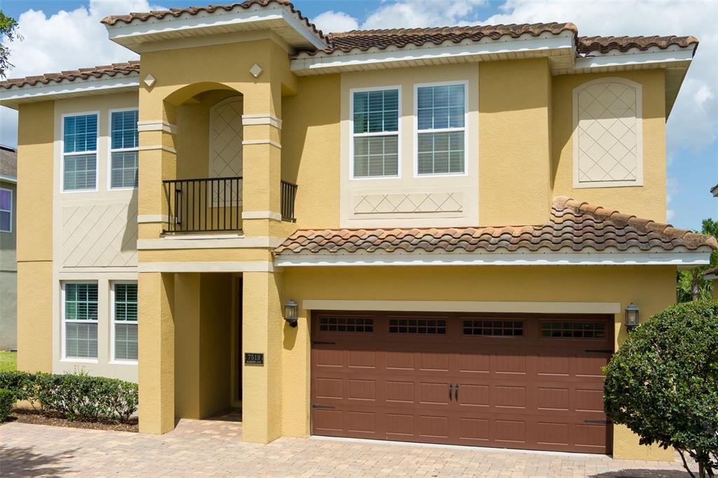 A two-story yellow stucco house with a brown garage door and a tiled roof — 7519 MARKER AVENUE, KISSIMMEE, FL