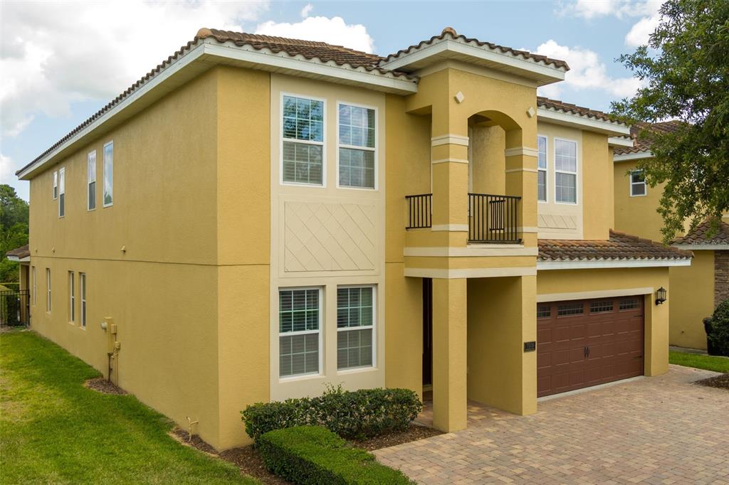 A two-story yellow stucco house features a brown garage door and a small upper balcony — 7519 MARKER AVENUE, KISSIMMEE, FL