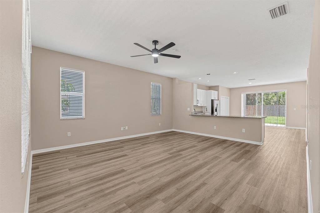 An open-concept living area features light-colored walls, wood-look flooring, a ceiling fan, and a kitchen — 12737 BRAMFIELD DRIVE, RIVERVIEW, FL