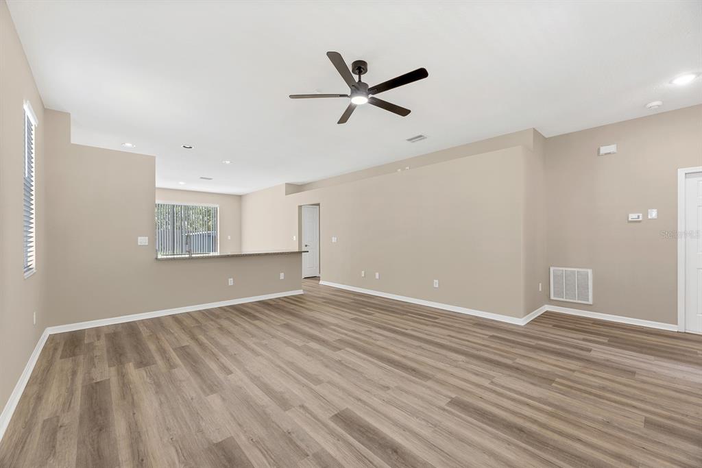An empty living room with light-colored walls, wood-look flooring, a ceiling fan, and a breakfast bar — 12737 BRAMFIELD DRIVE, RIVERVIEW, FL