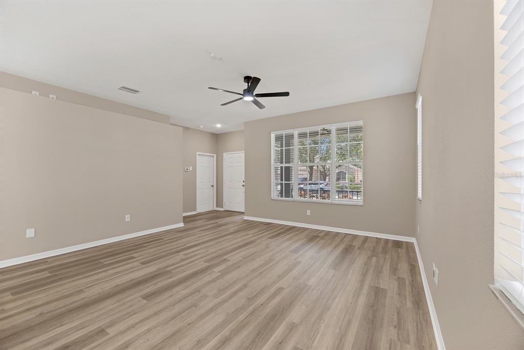 An empty room with light-colored walls, wood-look flooring, a ceiling fan, and large windows — 12737 BRAMFIELD DRIVE, RIVERVIEW, FL