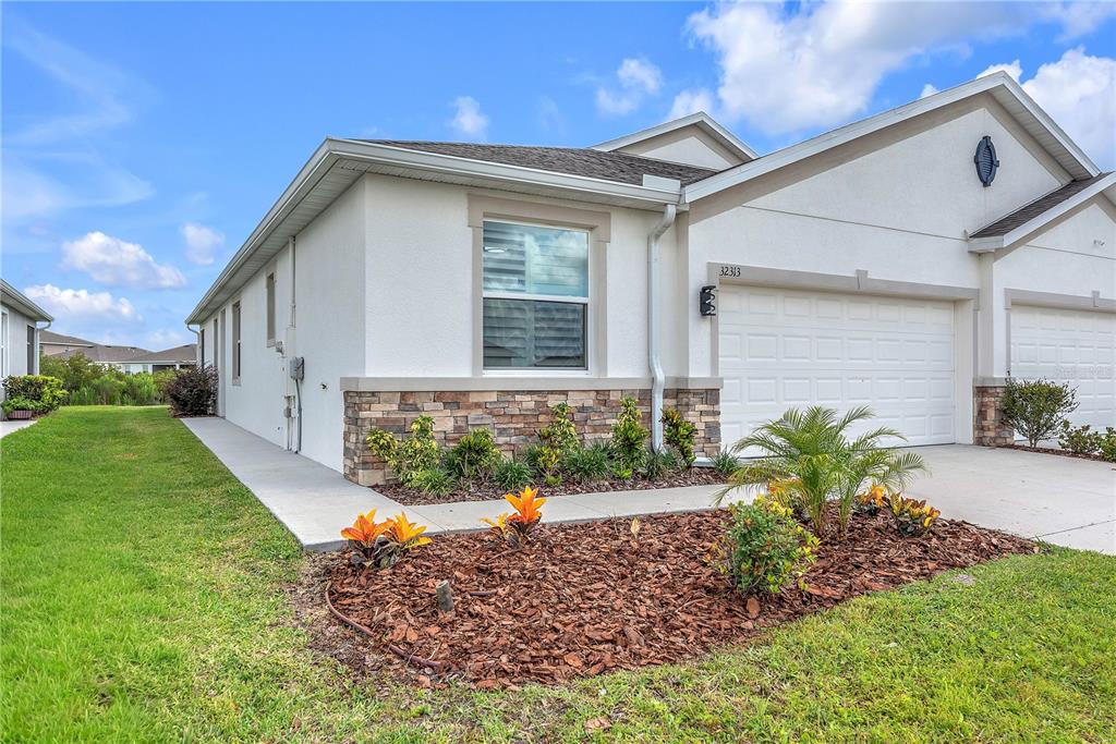 A single-story house exterior features white stucco walls, stone accents, and a two-car garage — 32313 LEXINGTON STREET, WESLEY CHAPEL, FL