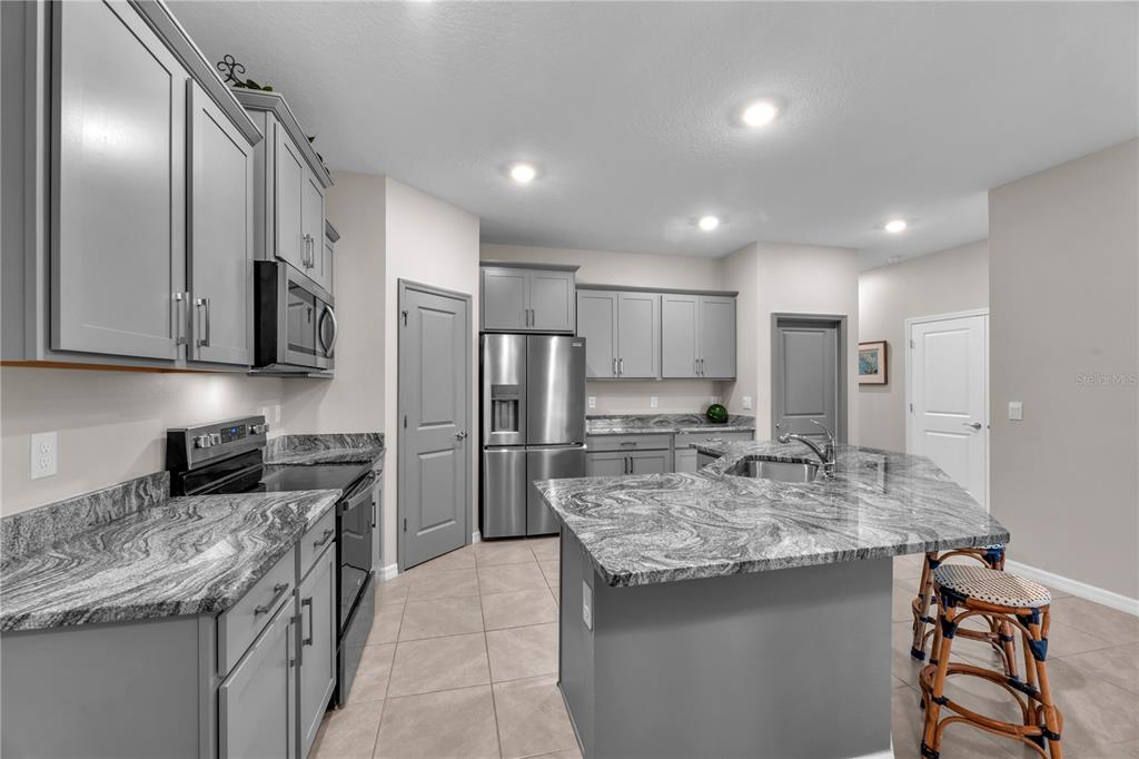 A kitchen features grey cabinets, granite countertops, stainless steel appliances, and a central island — 32313 LEXINGTON STREET, WESLEY CHAPEL, FL