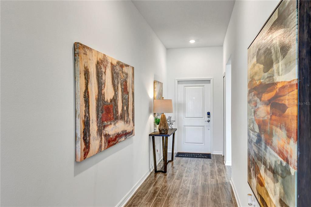 A bright entryway features wood-look tile flooring, two large abstract paintings, and a console table — 1328 TUPELO TRAIL, HAINES CITY, FL
