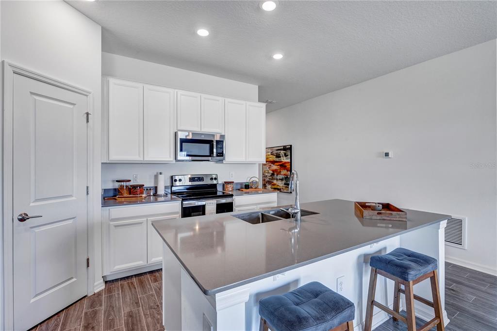 A modern kitchen features white cabinets, a gray island countertop, and two blue bar stools — 1328 TUPELO TRAIL, HAINES CITY, FL