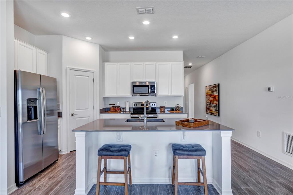 A kitchen features white cabinets, stainless steel appliances, a gray island, and two bar stools — 1328 TUPELO TRAIL, HAINES CITY, FL