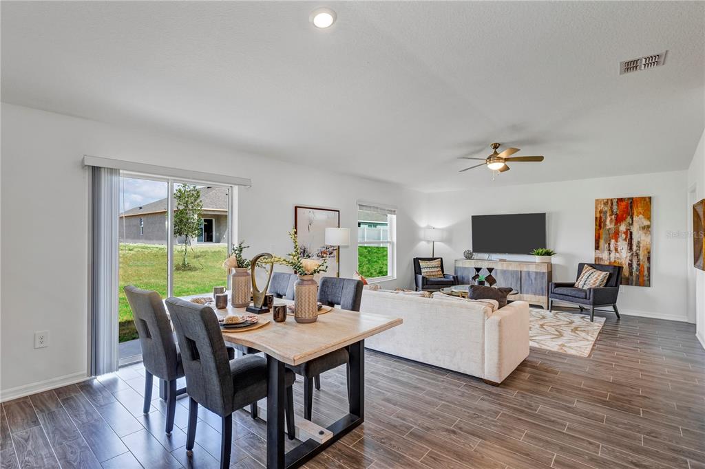 An open-concept living and dining area features wood-look tile flooring and a sliding glass door — 1328 TUPELO TRAIL, HAINES CITY, FL