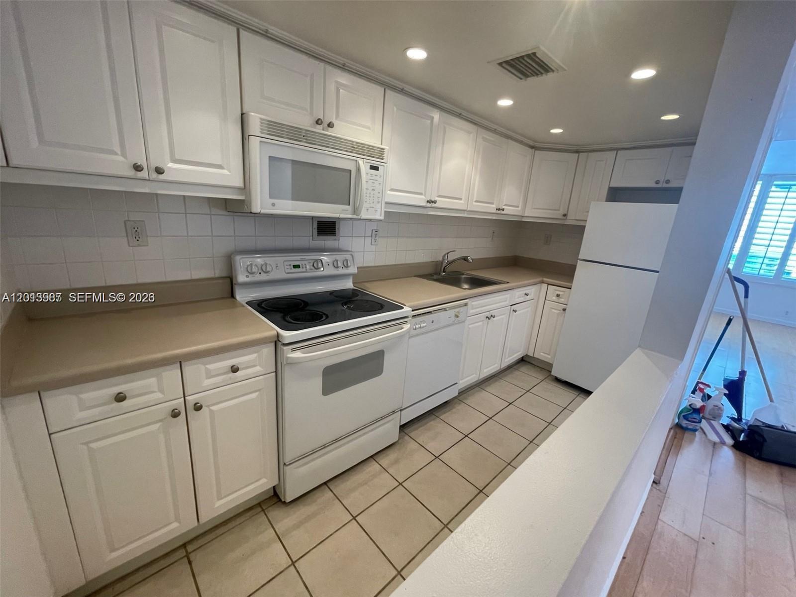 A kitchen features white cabinets, white appliances, tan countertops, and tiled flooring — 1000 West Ave # 1122, Miami Beach FL 33139, MIAMI BEACH, FL