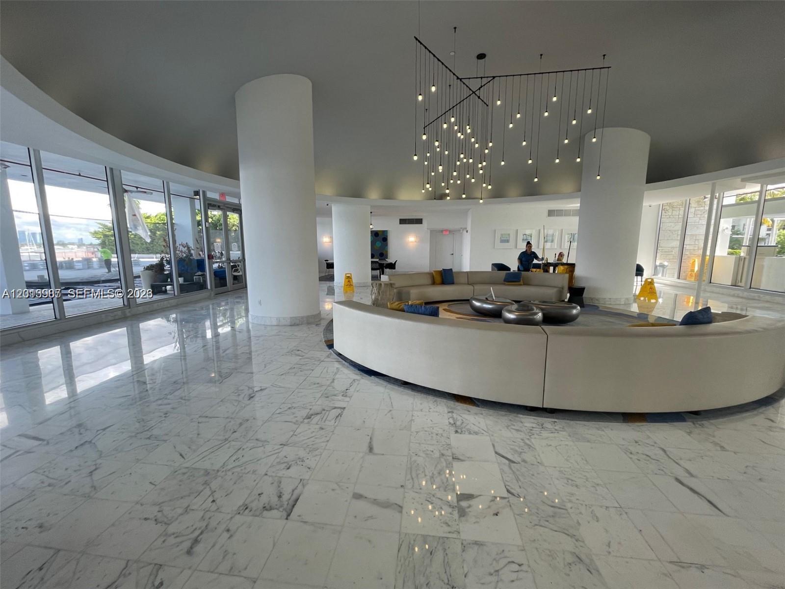 A spacious lobby features a curved sofa, marble flooring, large columns, and a modern chandelier — 1000 West Ave # 1122, Miami Beach FL 33139, MIAMI BEACH, FL