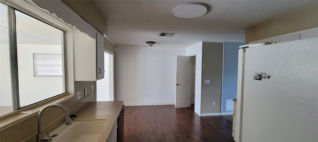 A kitchen with a sink, white cabinets, and a refrigerator overlooking an adjacent living area — 1425 NE OLD MILL DRIVE, DELTONA, FL