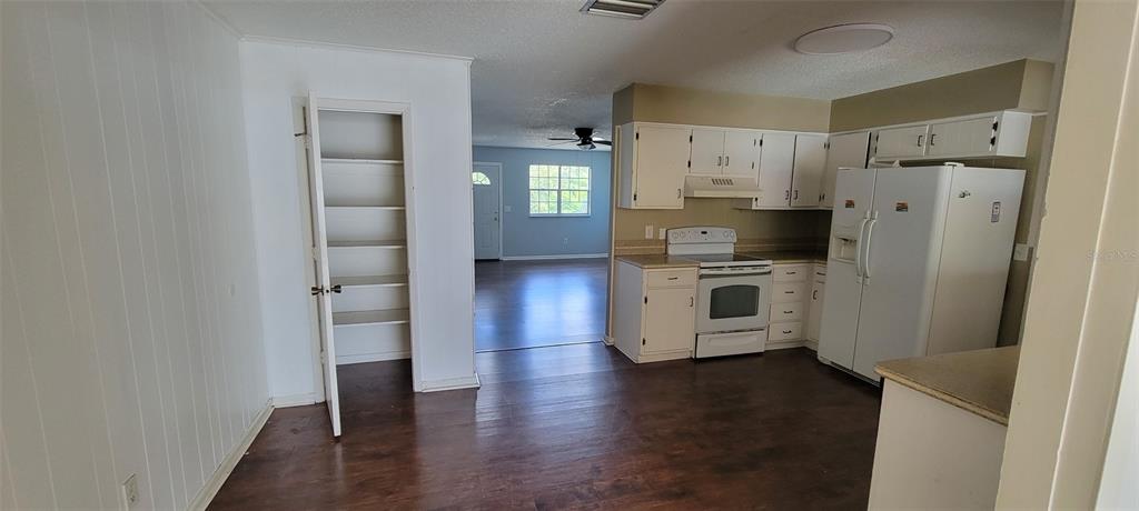A kitchen with white cabinets and appliances opens into a living area with wood flooring — 1425 NE OLD MILL DRIVE, DELTONA, FL
