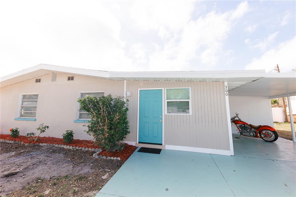 A single-story house with a teal front door, light-colored siding, and a covered carport — 300 53RD STREET W, BRADENTON, FL