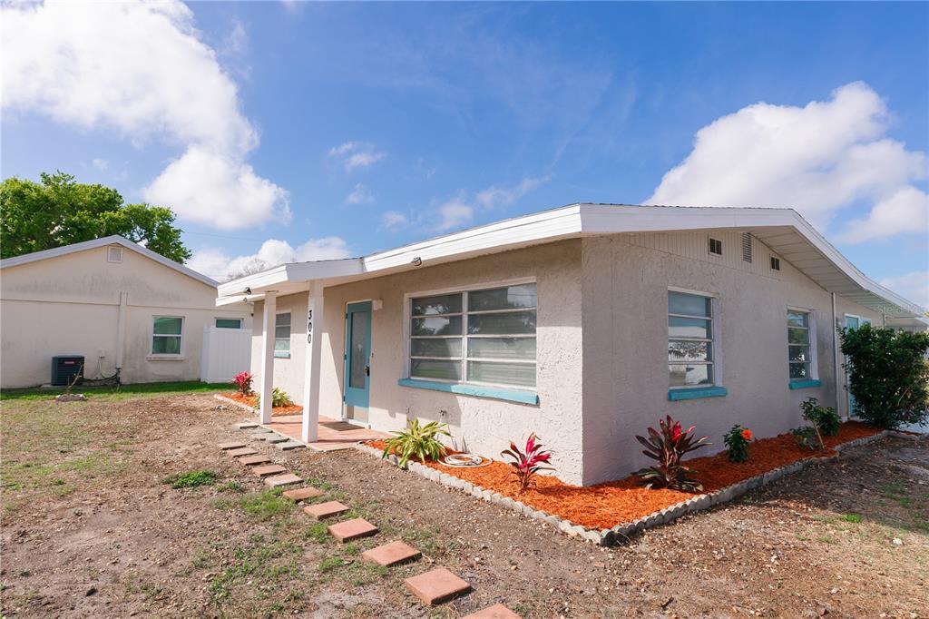 A single-story house with light-colored stucco walls, a blue door, and a stone walkway — 300 53RD STREET W, BRADENTON, FL