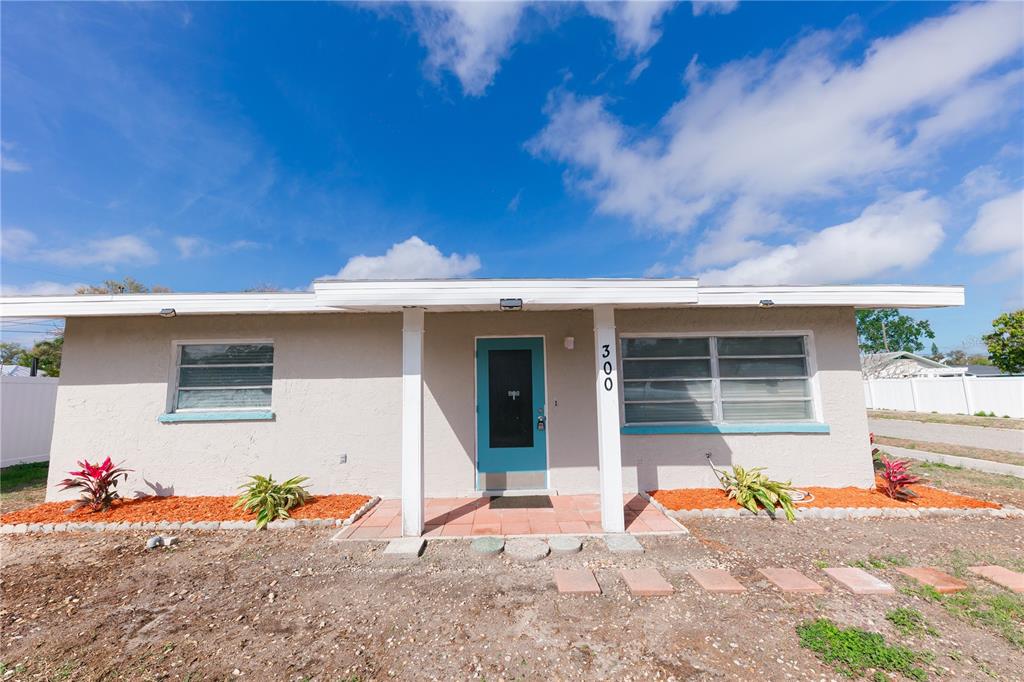 A single-story house features a light-colored stucco exterior, a turquoise front door, and orange mulch — 300 53RD STREET W, BRADENTON, FL