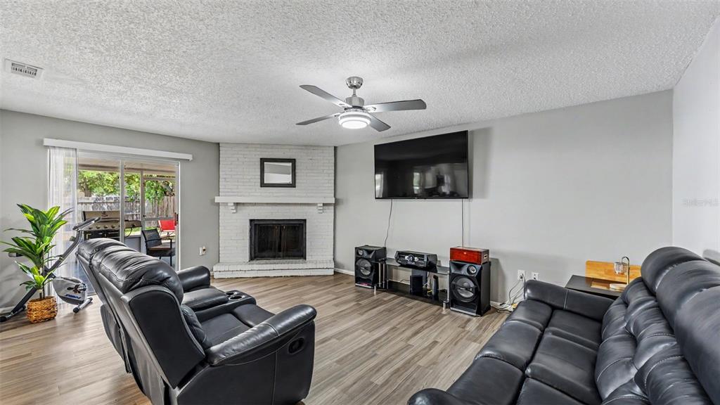 A living room features a white brick corner fireplace, a wall-mounted television, and wood flooring — 1309 CINNAMON WAY W, LAKELAND, FL