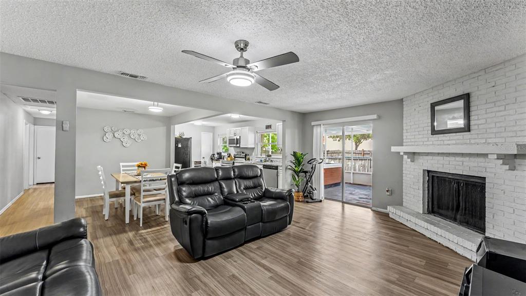 A living room with wood-look flooring, a white brick fireplace, and an adjacent dining area — 1309 CINNAMON WAY W, LAKELAND, FL