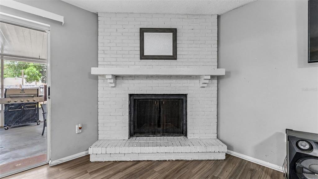 A white brick fireplace with a wooden mantel sits between a sliding glass door and wall — 1309 CINNAMON WAY W, LAKELAND, FL