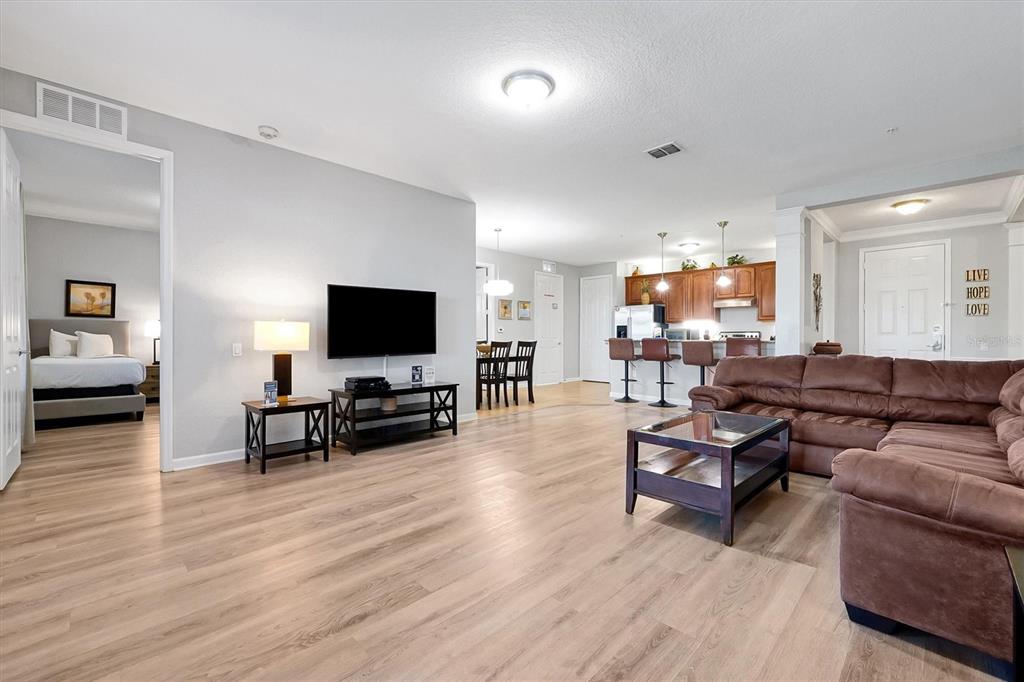 A living room with light wood floors, a brown sectional sofa, and an open kitchen — 5048 SHOREWAY LOOP UNIT 10204, ORLANDO, FL