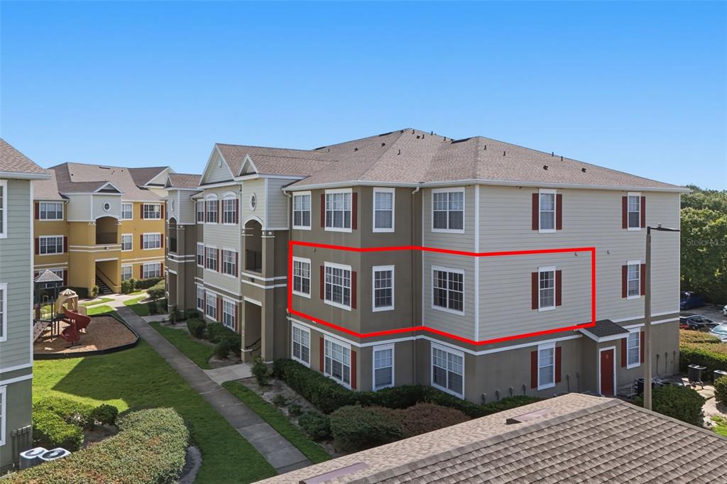 An exterior view of a multi-story apartment building with a red outline highlighting a unit — 8201 CLAIRE ANN DRIVE UNIT 203, ORLANDO, FL