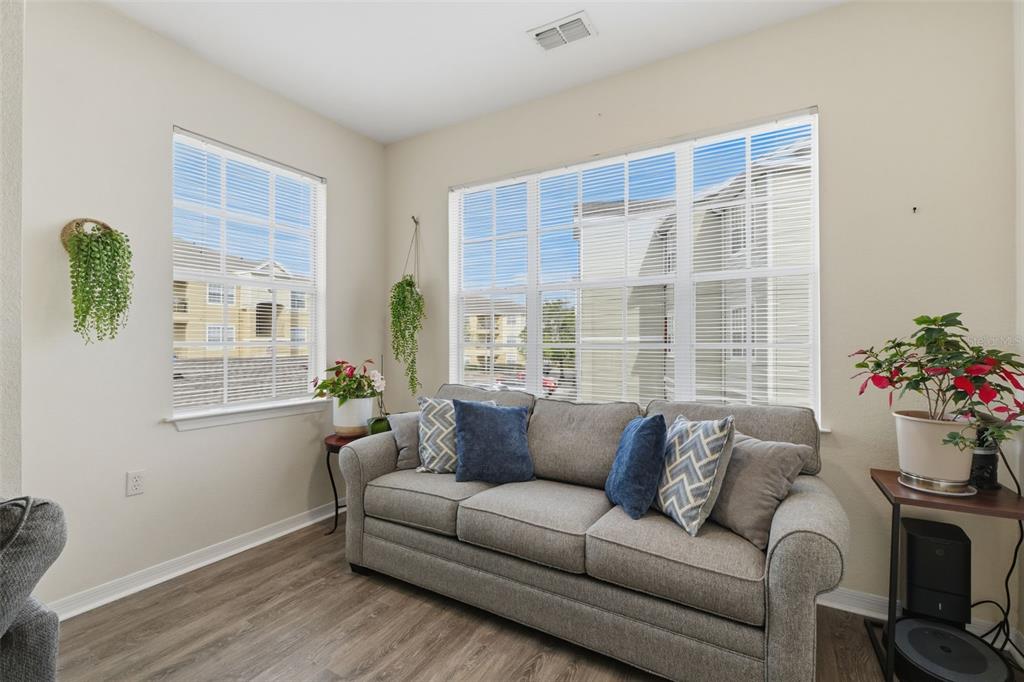 A living room features a gray sofa, wood-look flooring, and windows overlooking an apartment complex — 8201 CLAIRE ANN DRIVE UNIT 203, ORLANDO, FL