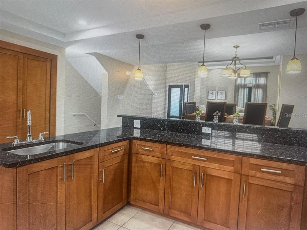 A kitchen features wooden cabinets, black granite countertops, and a breakfast bar with pendant lighting — 14519 DAMAI LANE, ORLANDO, FL