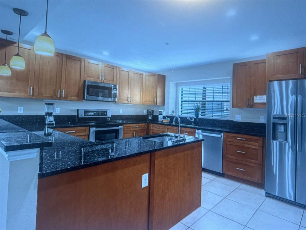 A kitchen features wooden cabinets, black granite countertops, stainless steel appliances, and a central island — 14519 DAMAI LANE, ORLANDO, FL