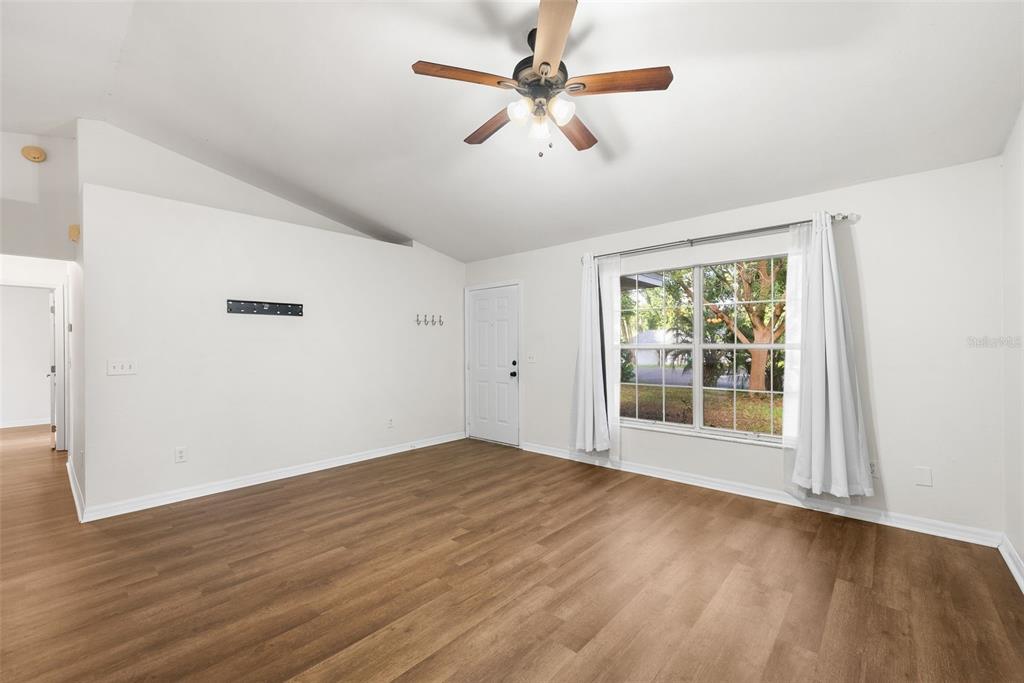 An empty room with wood-look flooring, a ceiling fan, and a window with white curtains — 19947 NW 245TH TERRACE, HIGH SPRINGS, FL
