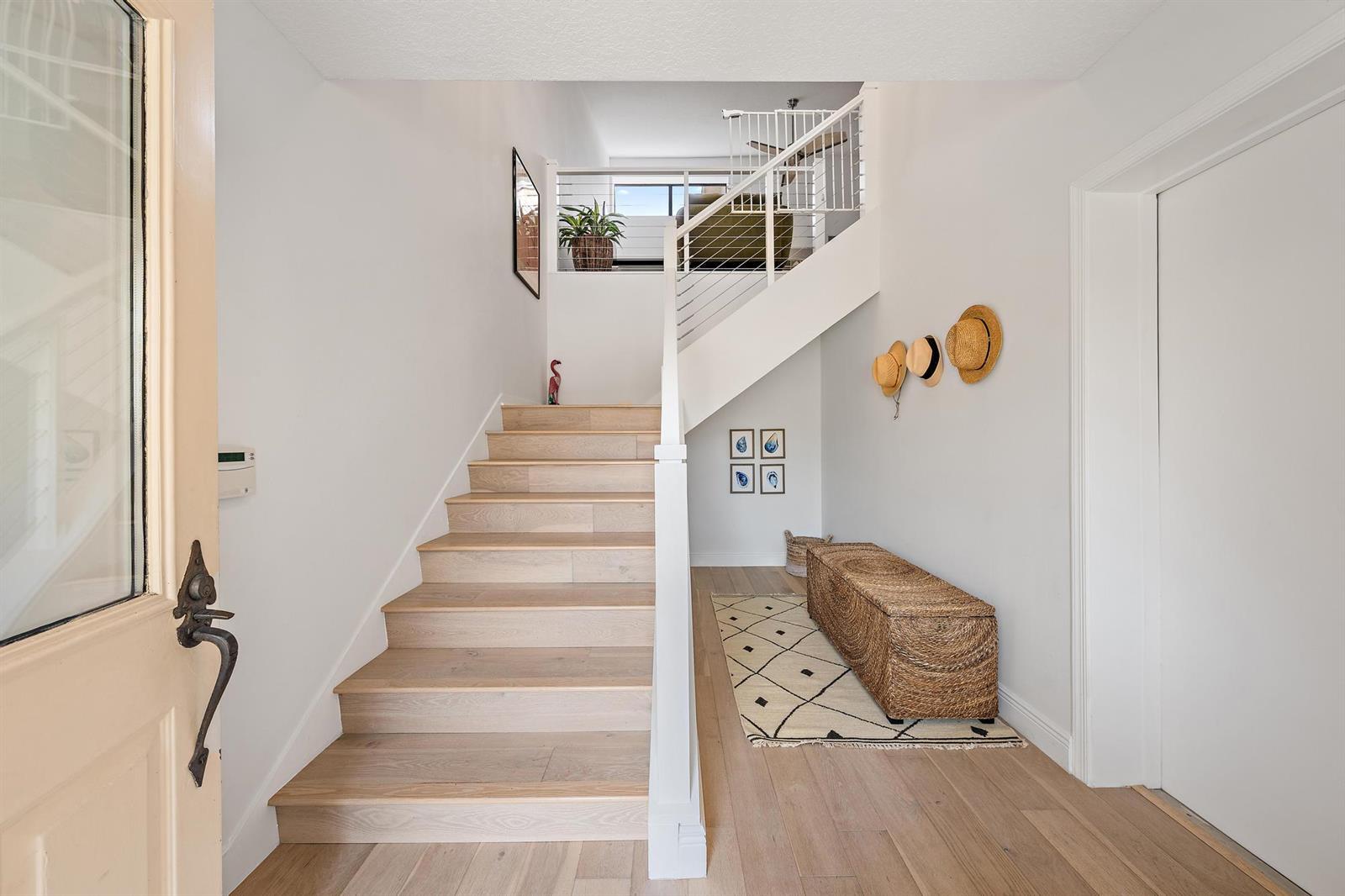 A bright entryway features light wood stairs, a woven bench, and a white staircase railing — 17165 Waterbend Drive # 206, Jupiter FL 33477, JUPITER, FL