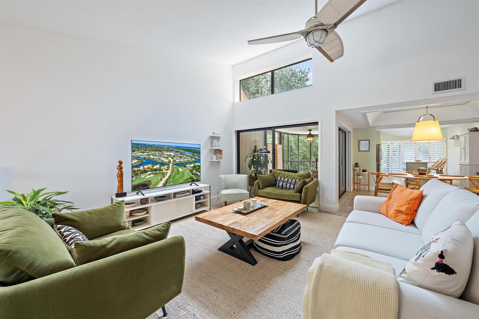 A bright living room features high ceilings, a green sofa, and a wooden coffee table — 17165 Waterbend Drive # 206, Jupiter FL 33477, JUPITER, FL