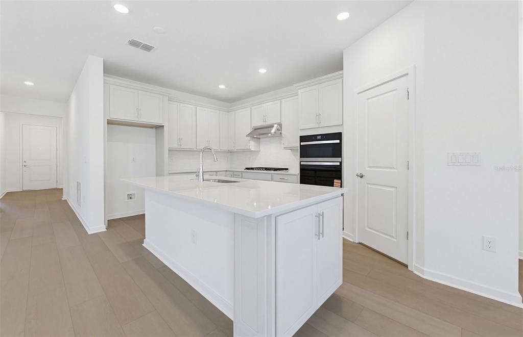 A modern kitchen features white cabinetry, a central island with a sink, and stainless appliances — 33425 HERDS HALLOW WAY, WESLEY CHAPEL, FL
