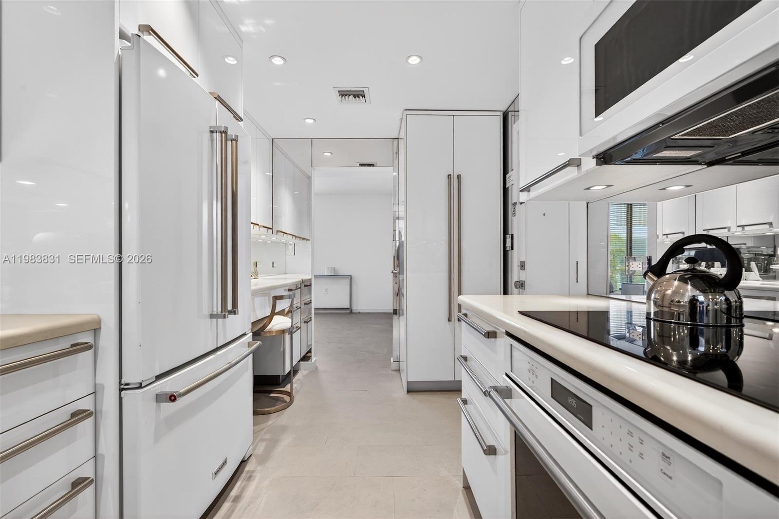 A modern galley kitchen features white high-gloss cabinetry, stainless steel hardware, and a tea kettle — 10178 Collins Ave # 208, Bal Harbour FL 33154, BAL HARBOUR, FL