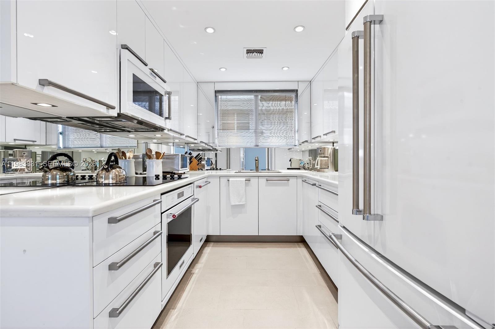 A modern, all-white galley kitchen features high-gloss cabinetry, stainless steel appliances, and tiled flooring — 10178 Collins Ave # 208, Bal Harbour FL 33154, BAL HARBOUR, FL