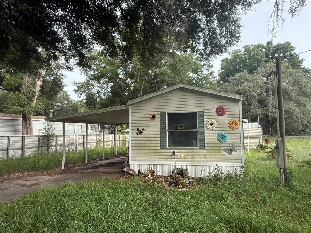 A single-story mobile home with a metal carport and decorative wall flowers on the exterior — 11184 SW 108TH STREET, DUNNELLON, FL