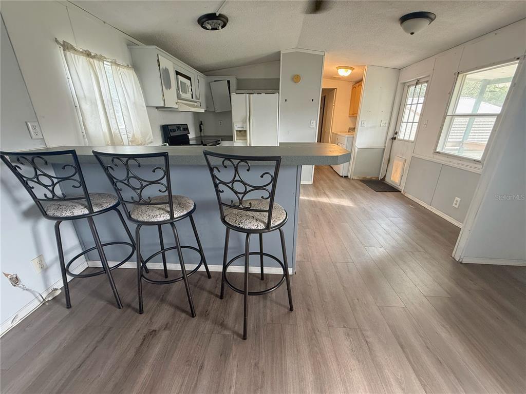 A kitchen with a breakfast bar, three stools, light gray walls, and wood-look flooring — 11184 SW 108TH STREET, DUNNELLON, FL