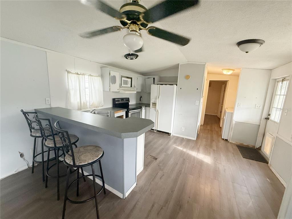 A kitchen with a breakfast bar, light-colored cabinets, white appliances, and wood-look flooring — 11184 SW 108TH STREET, DUNNELLON, FL