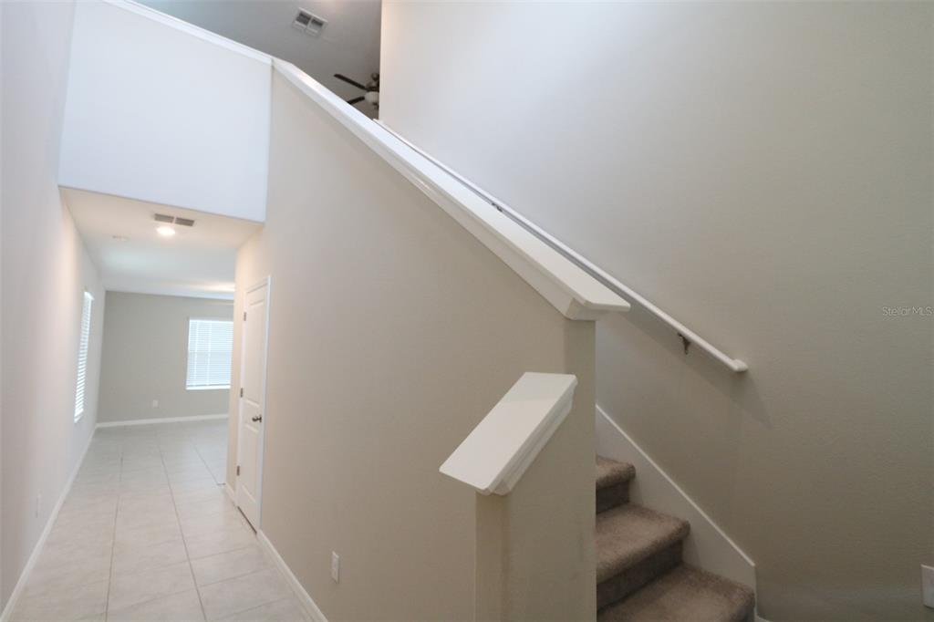 A carpeted staircase with a white handrail leads upward next to a tiled hallway — 3715 DAISY BLOOM PLACE, TAMPA, FL