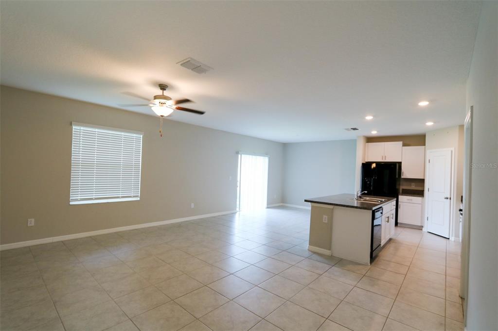 An open-concept living area features light tile flooring, a ceiling fan, and a kitchen island — 3715 DAISY BLOOM PLACE, TAMPA, FL