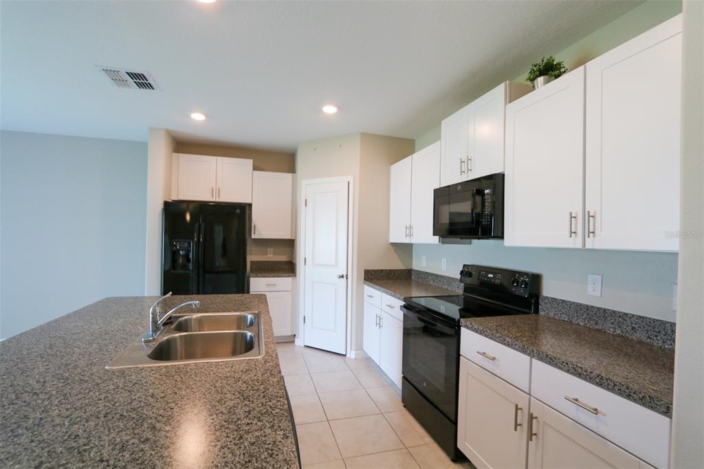 A kitchen features white cabinets, granite countertops, black appliances, and a central island with sink — 3715 DAISY BLOOM PLACE, TAMPA, FL