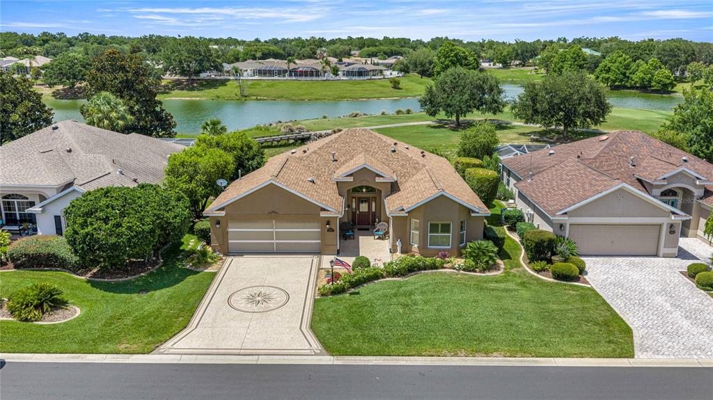 An aerial view shows a single-story house with a paved driveway and a backyard lake — 8481 SE 168TH KITTREDGE LOOP, THE VILLAGES, FL