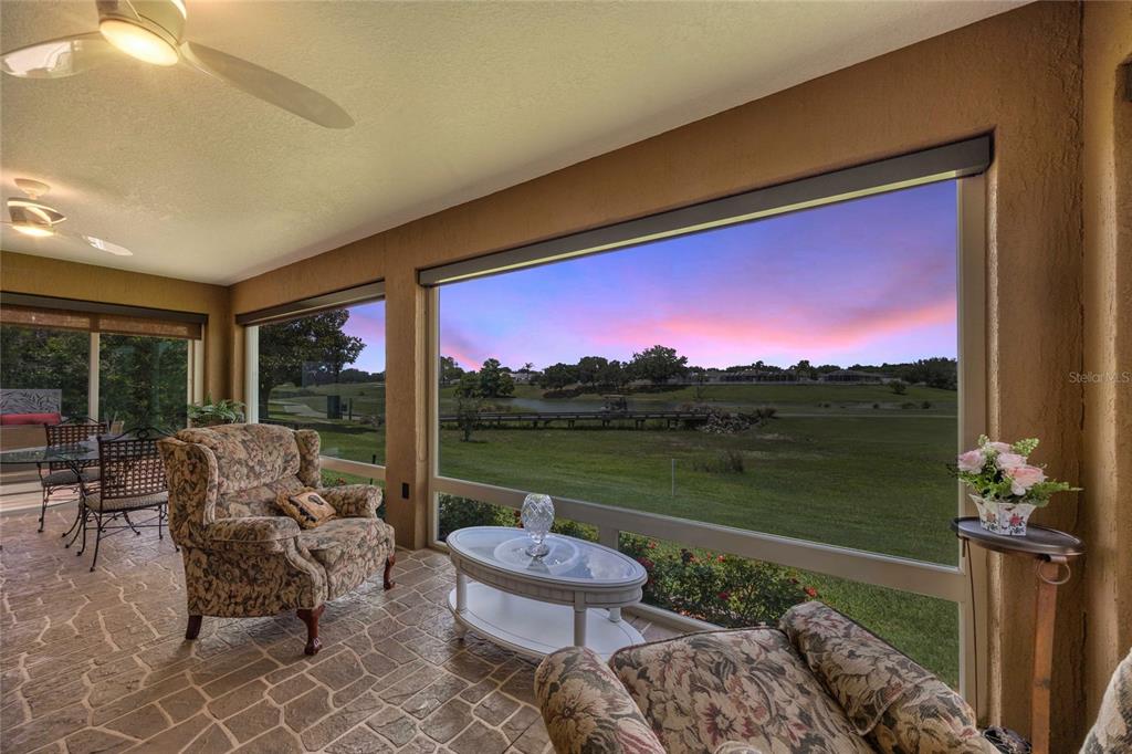 A sunroom with stone flooring and large windows overlooking a golf course at sunset — 8481 SE 168TH KITTREDGE LOOP, THE VILLAGES, FL