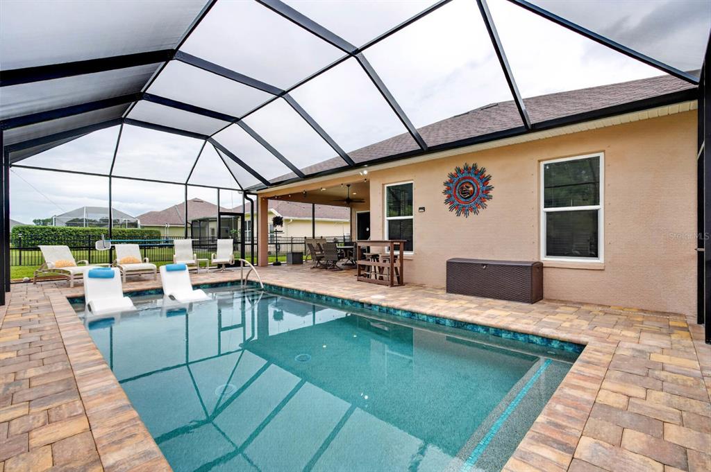 A screened-in patio features a rectangular swimming pool, lounge chairs, and a tan stucco wall — 3331 BELLINO BOULEVARD, NEW SMYRNA BEACH, FL