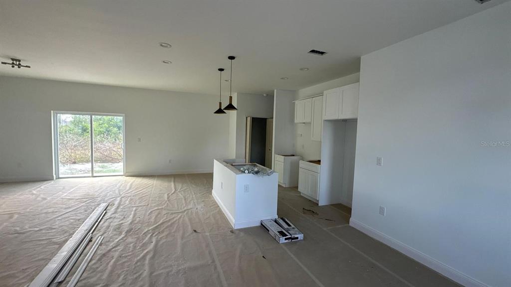 An unfinished kitchen area features white cabinets, a central island, and sliding glass doors — 12167 FLORENCE AVENUE, PORT CHARLOTTE, FL