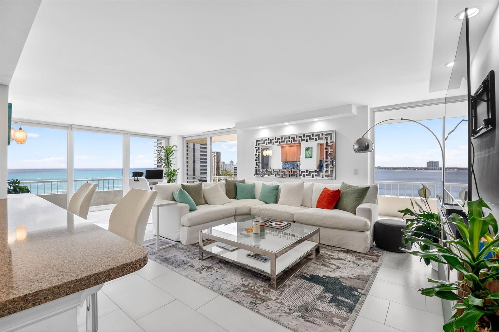 A bright living room features a white sectional sofa, glass coffee table, and ocean views — 5540 N Ocean Drive # 9b, Singer Island FL 33404, SINGER ISLAND, FL