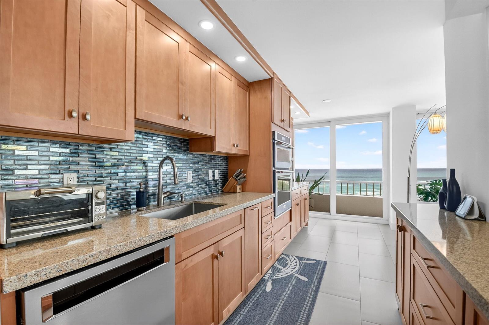 A kitchen with wood cabinets, granite countertops, a blue glass tile backsplash, and ocean views — 5540 N Ocean Drive # 9b, Singer Island FL 33404, SINGER ISLAND, FL