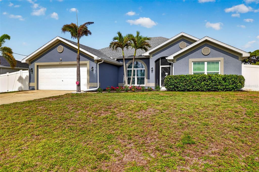 A blue single-story house with a two-car garage, palm trees, and a manicured lawn — 1417 NW 16TH PLACE, CAPE CORAL, FL