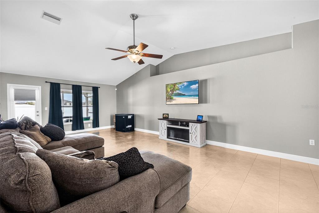A living room features a vaulted ceiling, tile flooring, a sectional sofa, and a wall-mounted television — 1417 NW 16TH PLACE, CAPE CORAL, FL