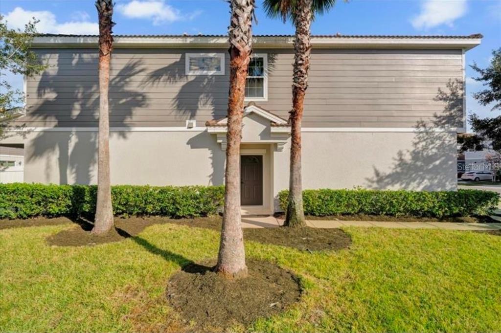 A gray front door is recessed under a covered entryway next to a palm tree — 9301 WATCHET WAY, ORLANDO, FL